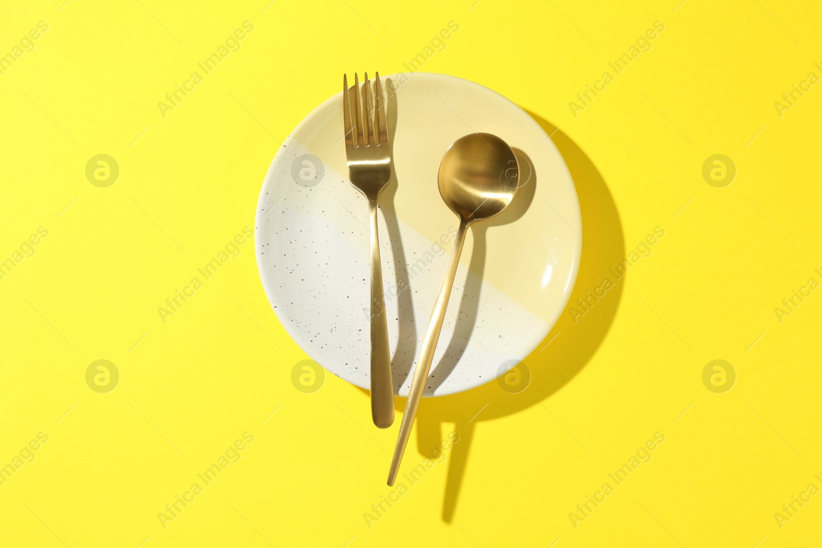 Stylish plate and cutlery on yellow background, top view Photo of Stylish plate and cutlery on yellow background, top view