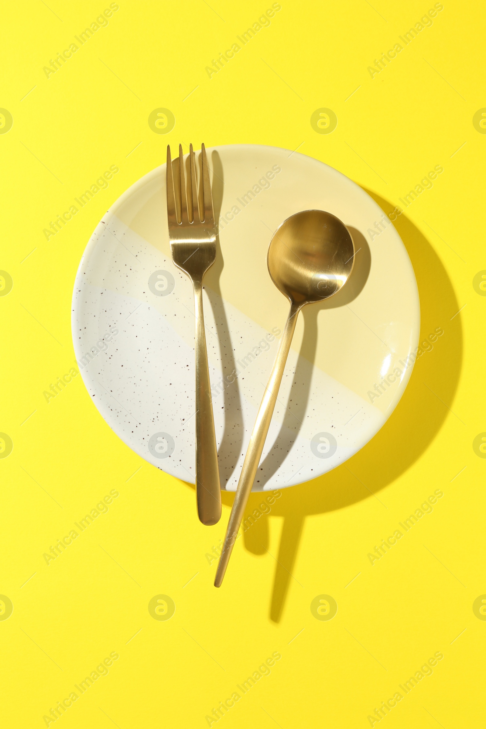 Stylish plate and cutlery on yellow background, top view Photo of Stylish plate and cutlery on yellow background, top view