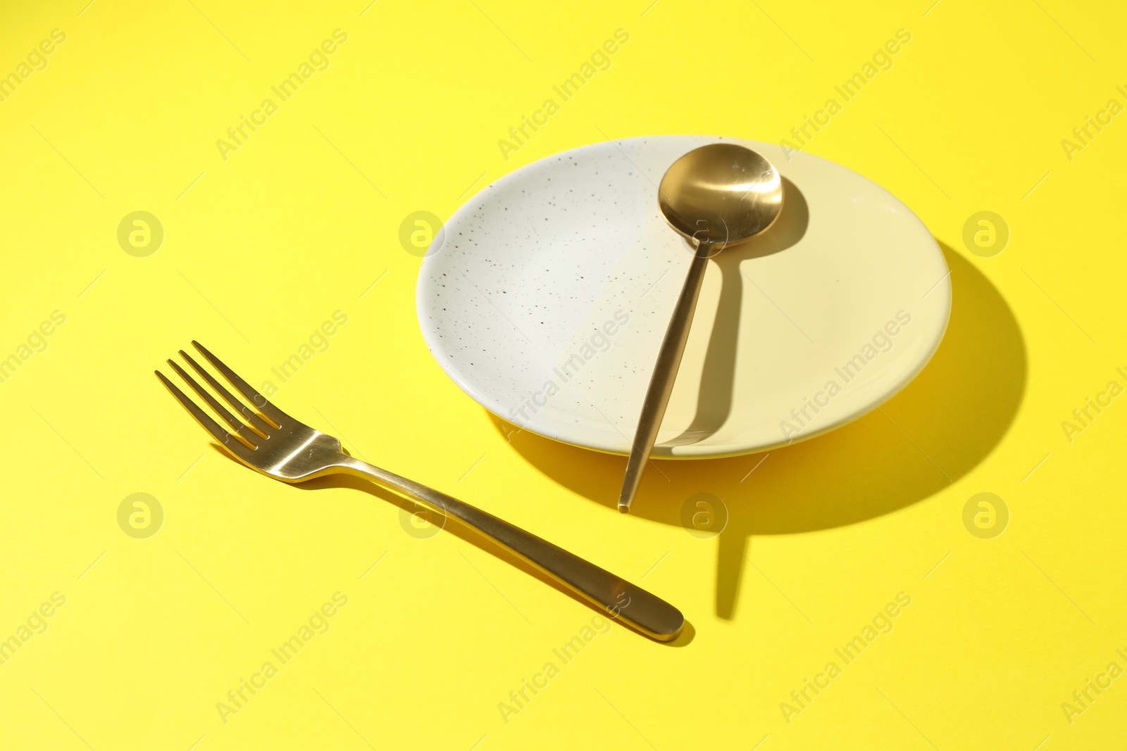 Stylish plate and cutlery on yellow background, closeup Photo of Stylish plate and cutlery on yellow background, closeup