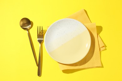 Photo of Stylish plate, cutlery and napkin on yellow background, flat lay