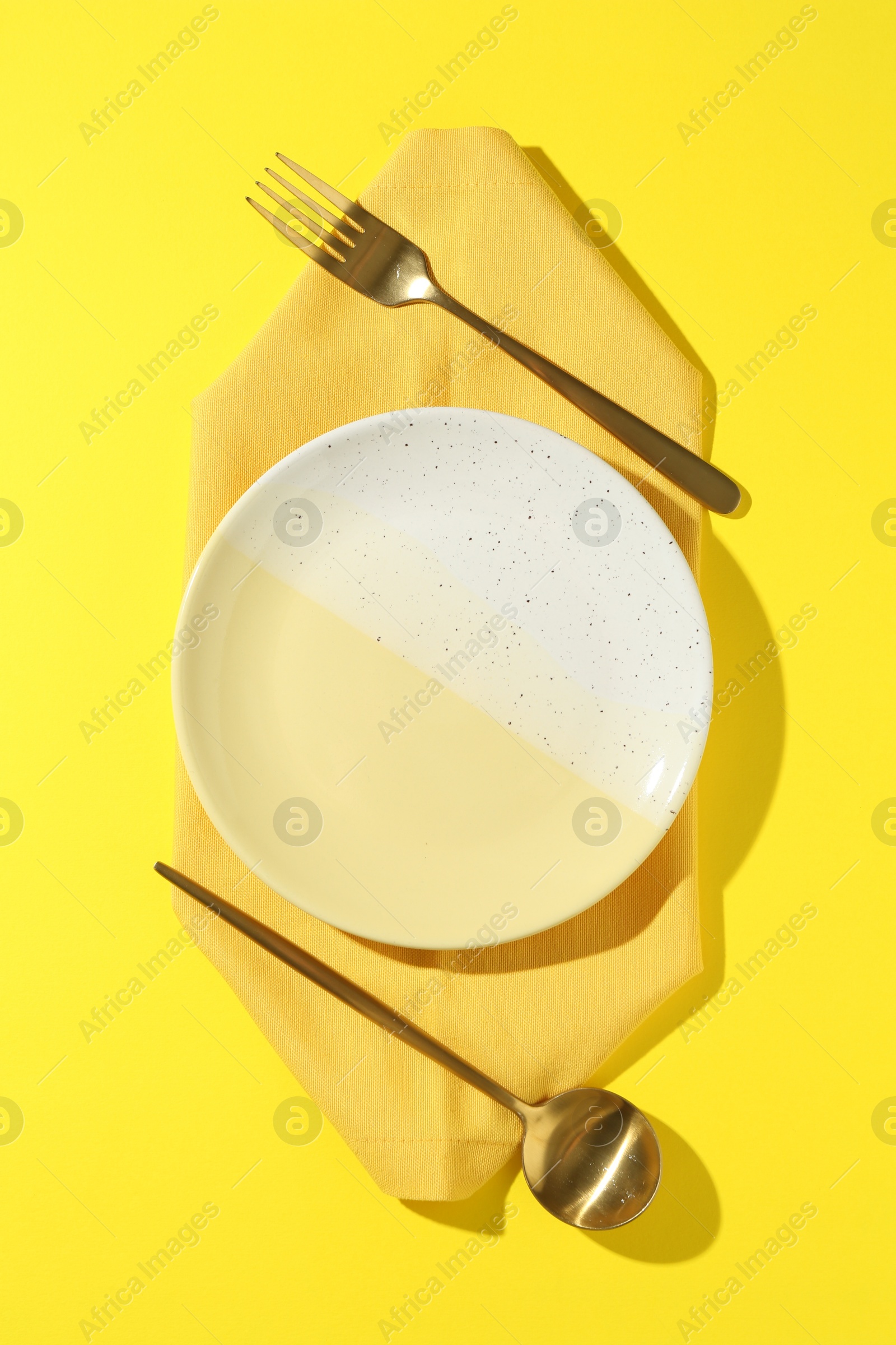 Stylish plate, cutlery and napkin on yellow background, flat lay Photo of Stylish plate, cutlery and napkin on yellow background, flat lay