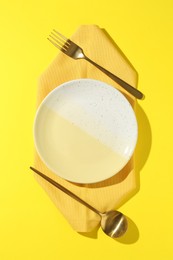 Photo of Stylish plate, cutlery and napkin on yellow background, flat lay