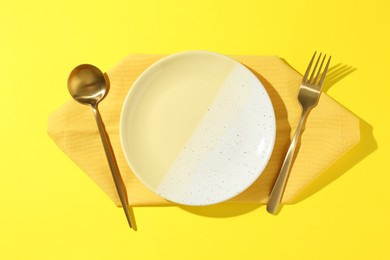 Photo of Stylish plate, cutlery and napkin on yellow background, flat lay