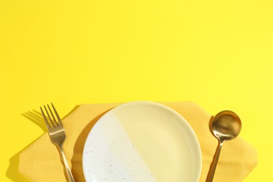Photo of Stylish plate, cutlery and napkin on yellow background, flat lay. Space for text