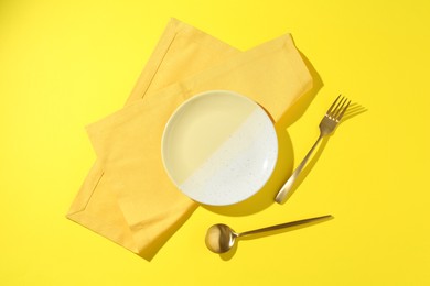 Photo of Stylish plate, cutlery and napkin on yellow background, flat lay
