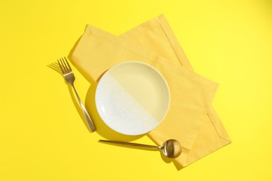 Photo of Stylish plate, cutlery and napkin on yellow background, flat lay