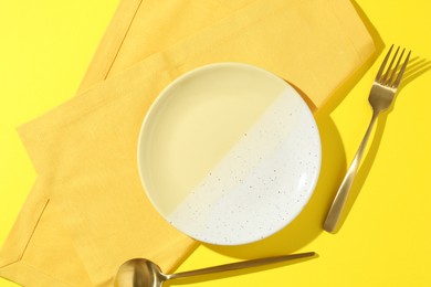 Photo of Stylish plate, cutlery and napkin on yellow background, flat lay