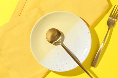 Photo of Stylish plate, cutlery and napkin on yellow background, flat lay