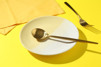 Photo of Stylish plate, cutlery and napkin on yellow background, closeup
