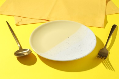 Photo of Stylish plate, cutlery and napkin on yellow background, closeup
