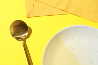 Photo of Stylish plate, spoon and napkin on yellow background, flat lay