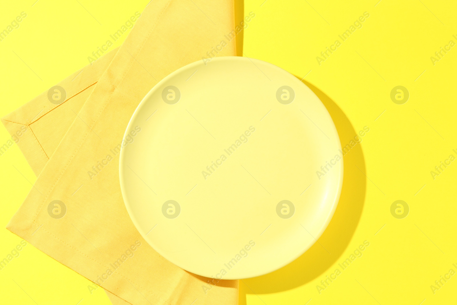 Stylish plate and napkin on yellow background, top view Photo of Stylish plate and napkin on yellow background, top view
