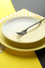 Photo of Stylish plates, fork and napkin on color background, closeup