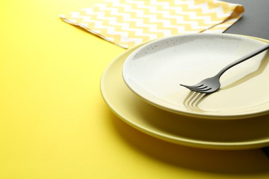 Photo of Stylish plates, fork and napkin on color background, closeup. Space for text