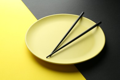 Photo of Stylish plate and chopsticks on color background, closeup