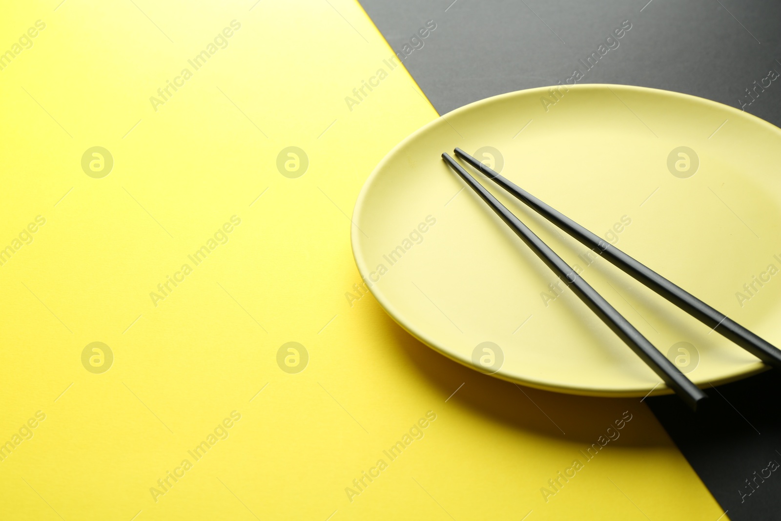 Stylish plate and chopsticks on color background, closeup. Space for text Photo of Stylish plate and chopsticks on color background, closeup. Space for text