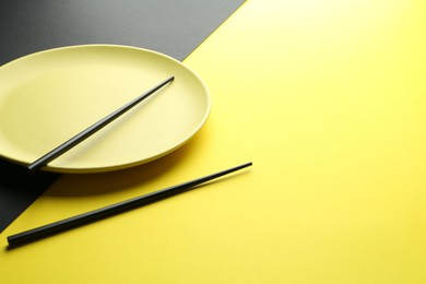 Photo of Stylish plate and chopsticks on color background, closeup. Space for text