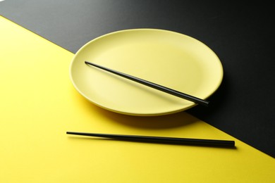 Photo of Stylish plate and chopsticks on color background, closeup