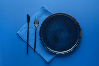 Photo of Stylish plate, cutlery and napkin on blue background, flat lay