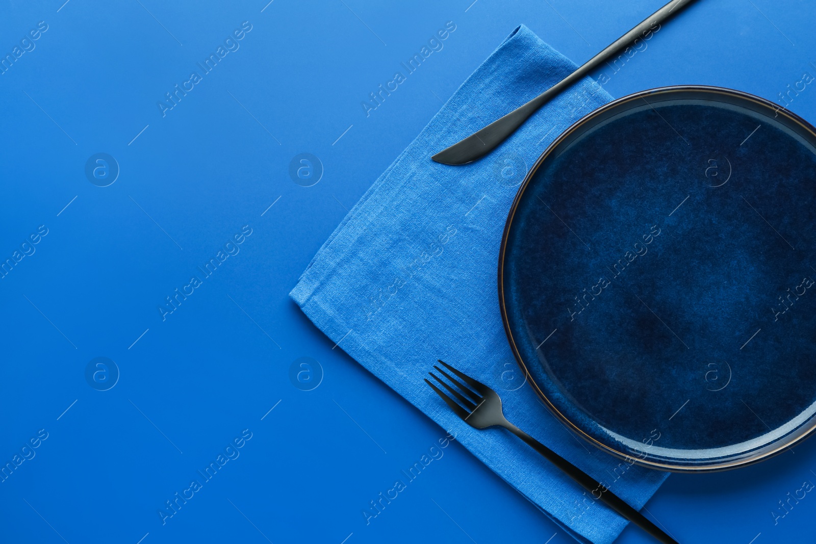 Stylish plate, cutlery and napkin on blue background, flat lay. Space for text Photo of Stylish plate, cutlery and napkin on blue background, flat lay. Space for text