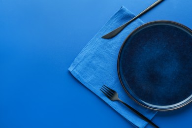 Photo of Stylish plate, cutlery and napkin on blue background, flat lay. Space for text