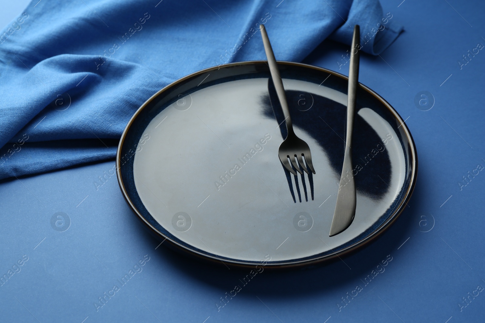 Stylish plate, cutlery and napkin on blue background, closeup Photo of Stylish plate, cutlery and napkin on blue background, closeup