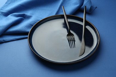 Photo of Stylish plate, cutlery and napkin on blue background, closeup