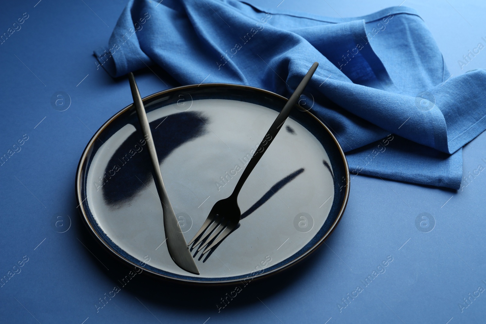Stylish plate, cutlery and napkin on blue background, closeup Photo of Stylish plate, cutlery and napkin on blue background, closeup
