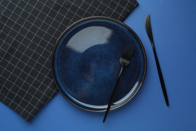 Photo of Stylish plate, cutlery and napkin on blue background, flat lay