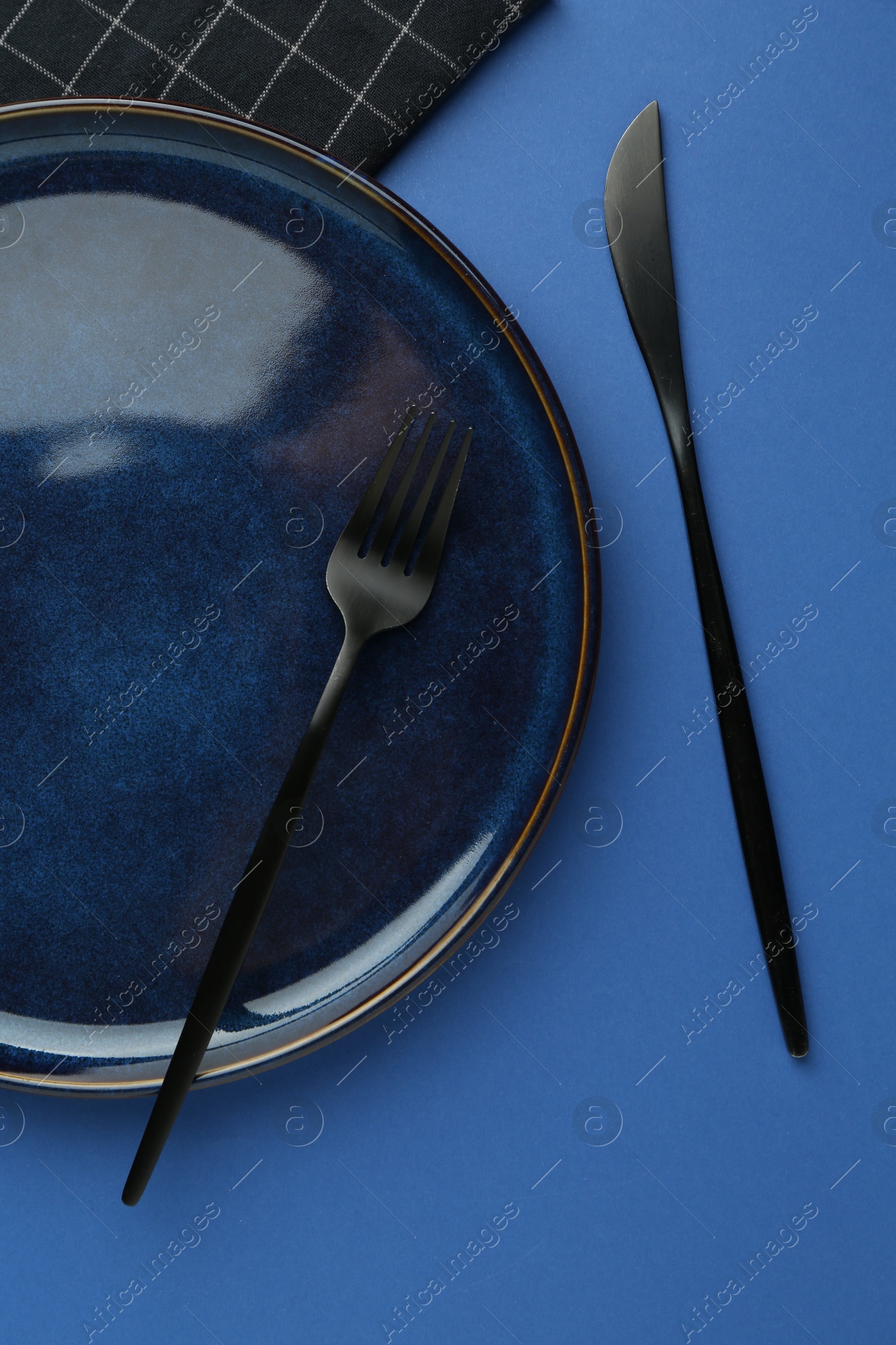 Stylish plate, cutlery and napkin on blue background, flat lay Photo of Stylish plate, cutlery and napkin on blue background, flat lay