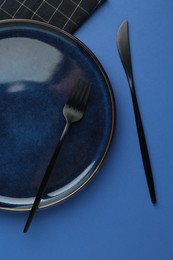 Photo of Stylish plate, cutlery and napkin on blue background, flat lay