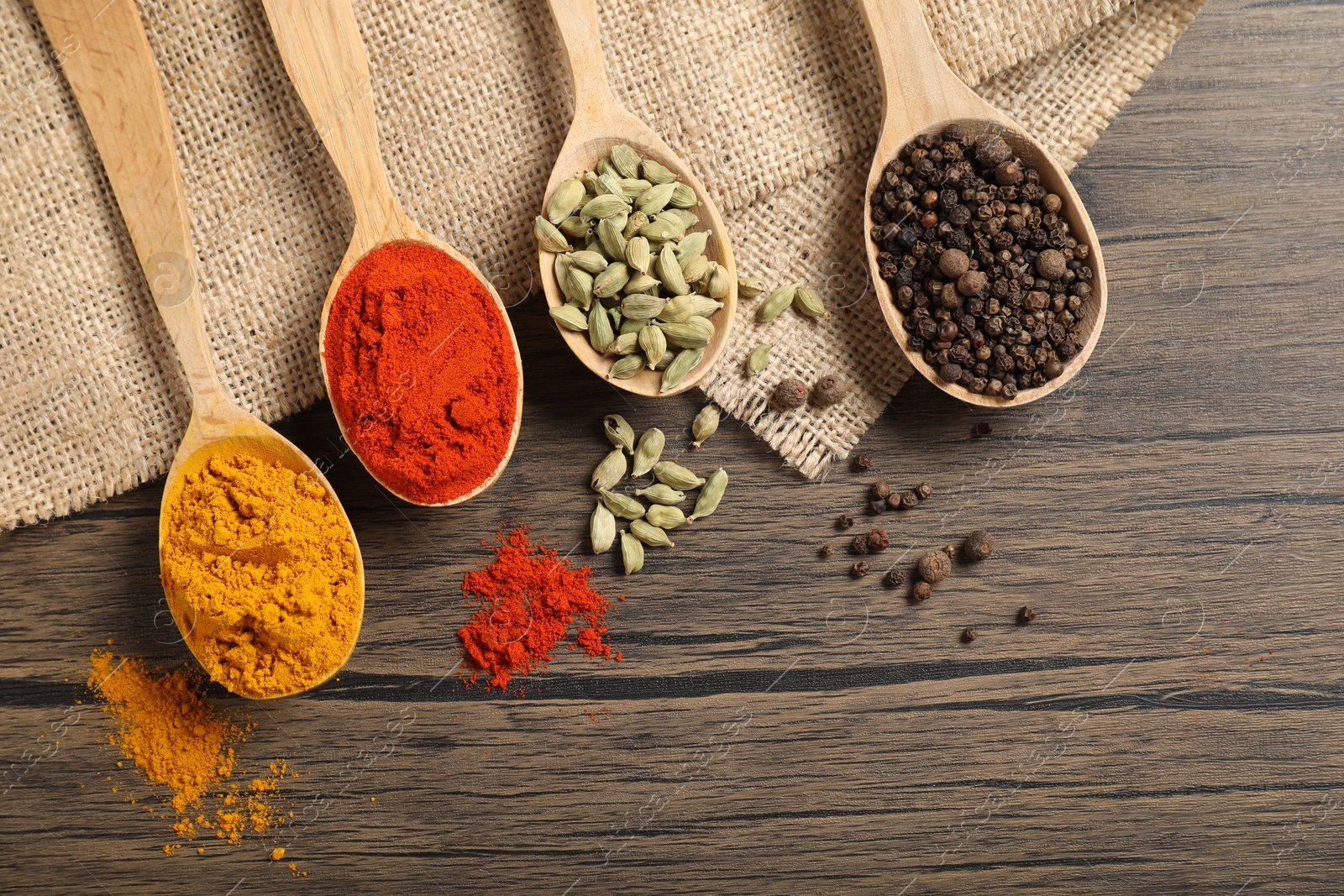 Photo of Different aromatic spices in spoons on wooden table, flat lay