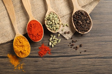 Photo of Different aromatic spices in spoons on wooden table, flat lay