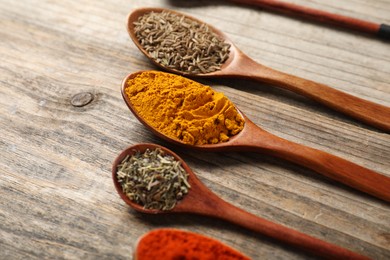 Photo of Different aromatic spices in spoons on wooden table, closeup