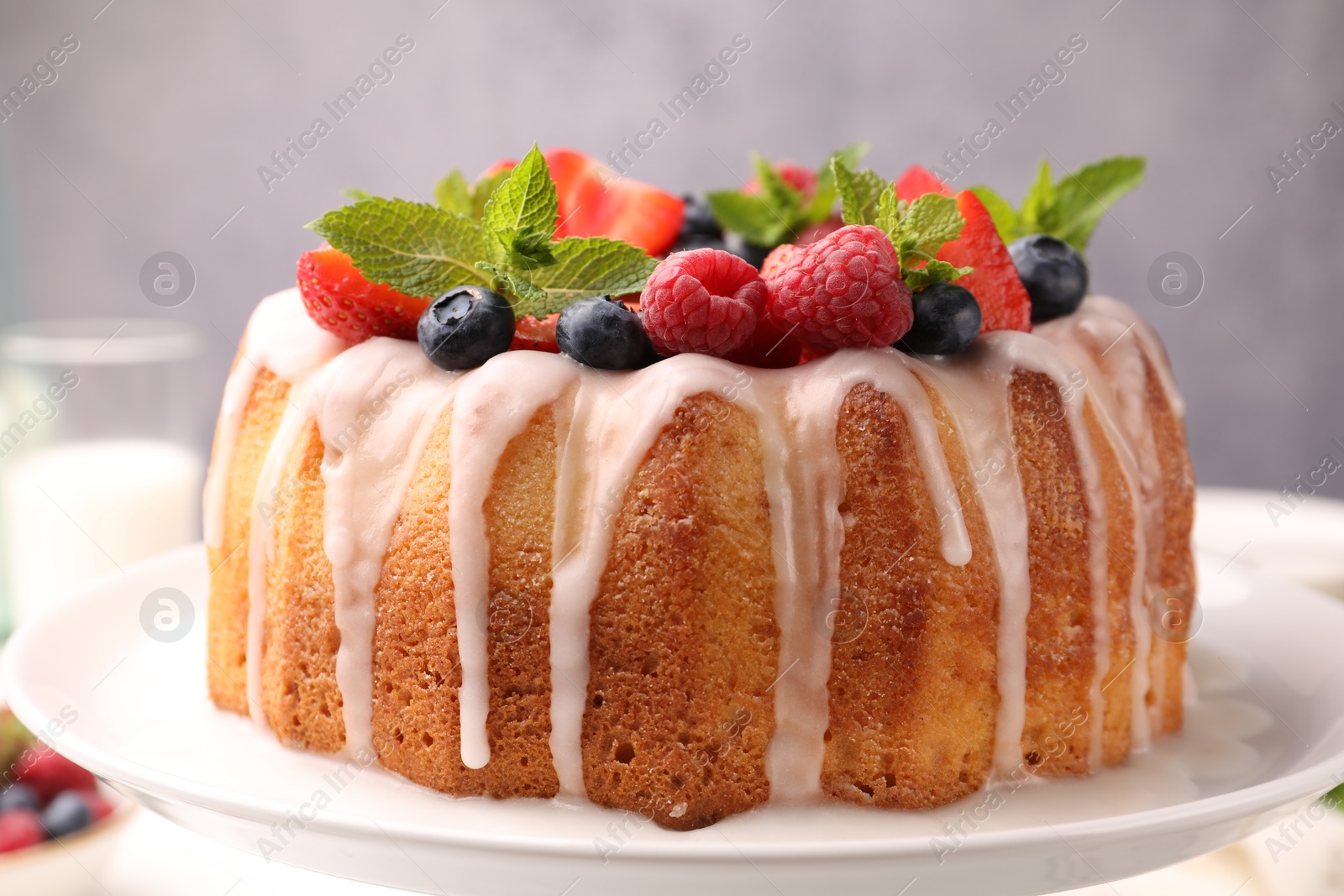 Delicious bundt cake with berries, glaze and mint on white table against grey background, closeup Photo of Delicious bundt cake with berries, glaze and mint on white table against grey background, closeup