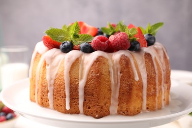 Photo of Delicious bundt cake with berries, glaze and mint on white table against grey background, closeup