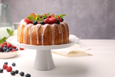 Photo of Delicious bundt cake with berries, glaze and mint on white wooden table against grey background, closeup