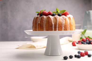 Photo of Delicious bundt cake with berries, glaze and mint on white wooden table against grey background, closeup