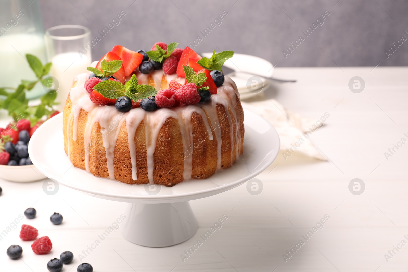 Delicious bundt cake with berries, glaze and mint on white wooden table against grey background, closeup Photo of Delicious bundt cake with berries, glaze and mint on white wooden table against grey background, closeup