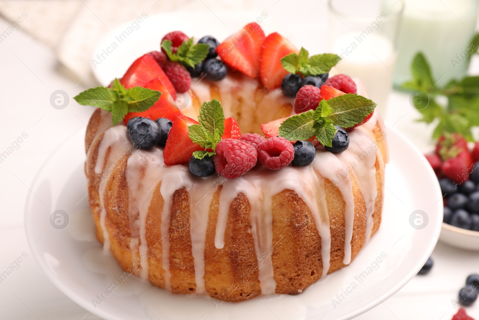 Delicious bundt cake with berries, glaze and mint on white table, closeup Photo of Delicious bundt cake with berries, glaze and mint on white table, closeup