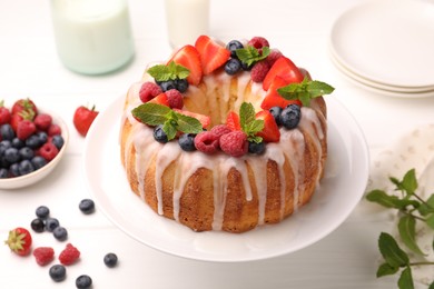 Photo of Delicious bundt cake with berries, glaze and mint on white wooden table, closeup