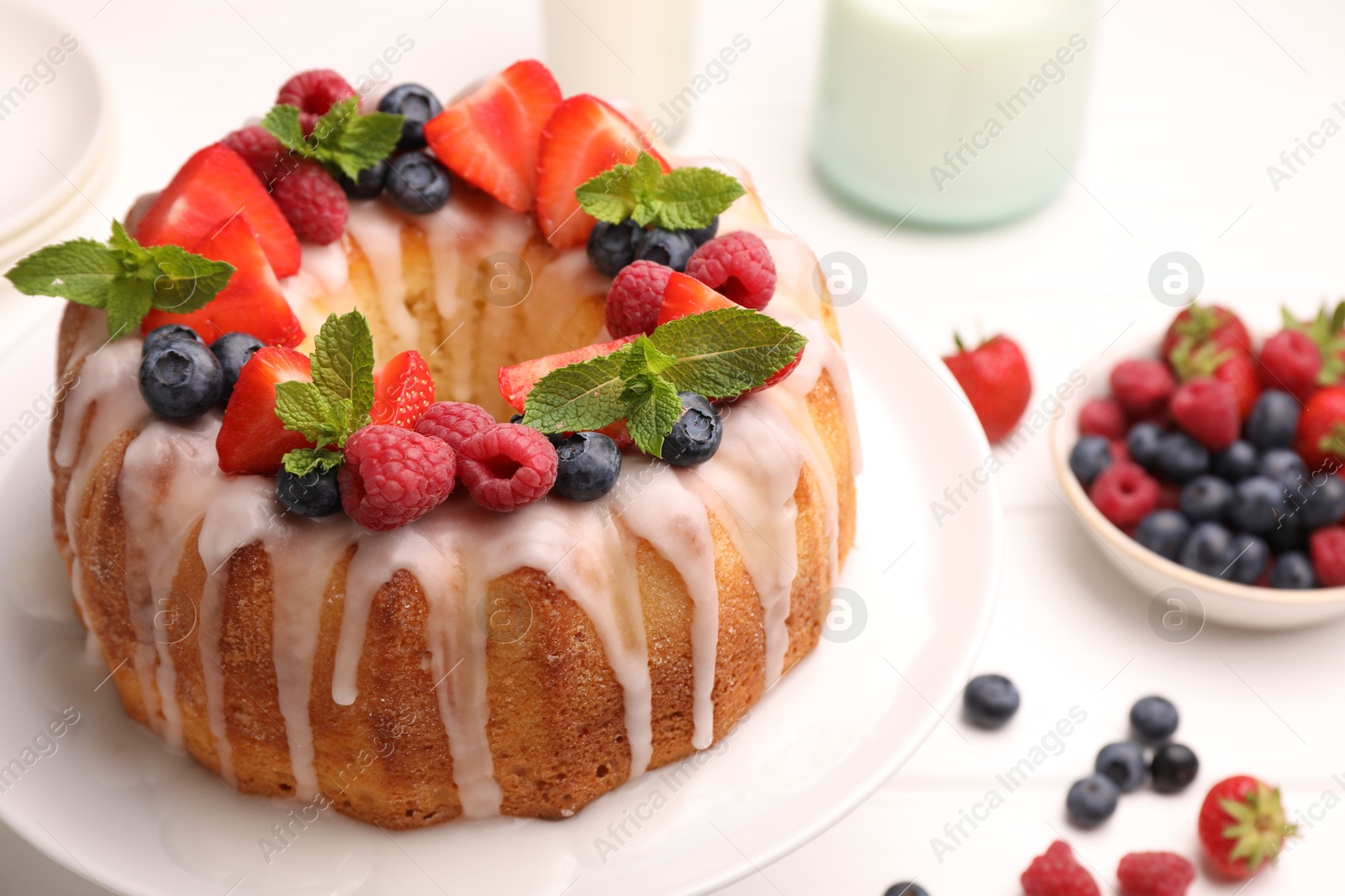Photo of Delicious bundt cake with berries, glaze and mint on white table, closeup