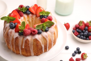 Photo of Delicious bundt cake with berries, glaze and mint on white table, closeup