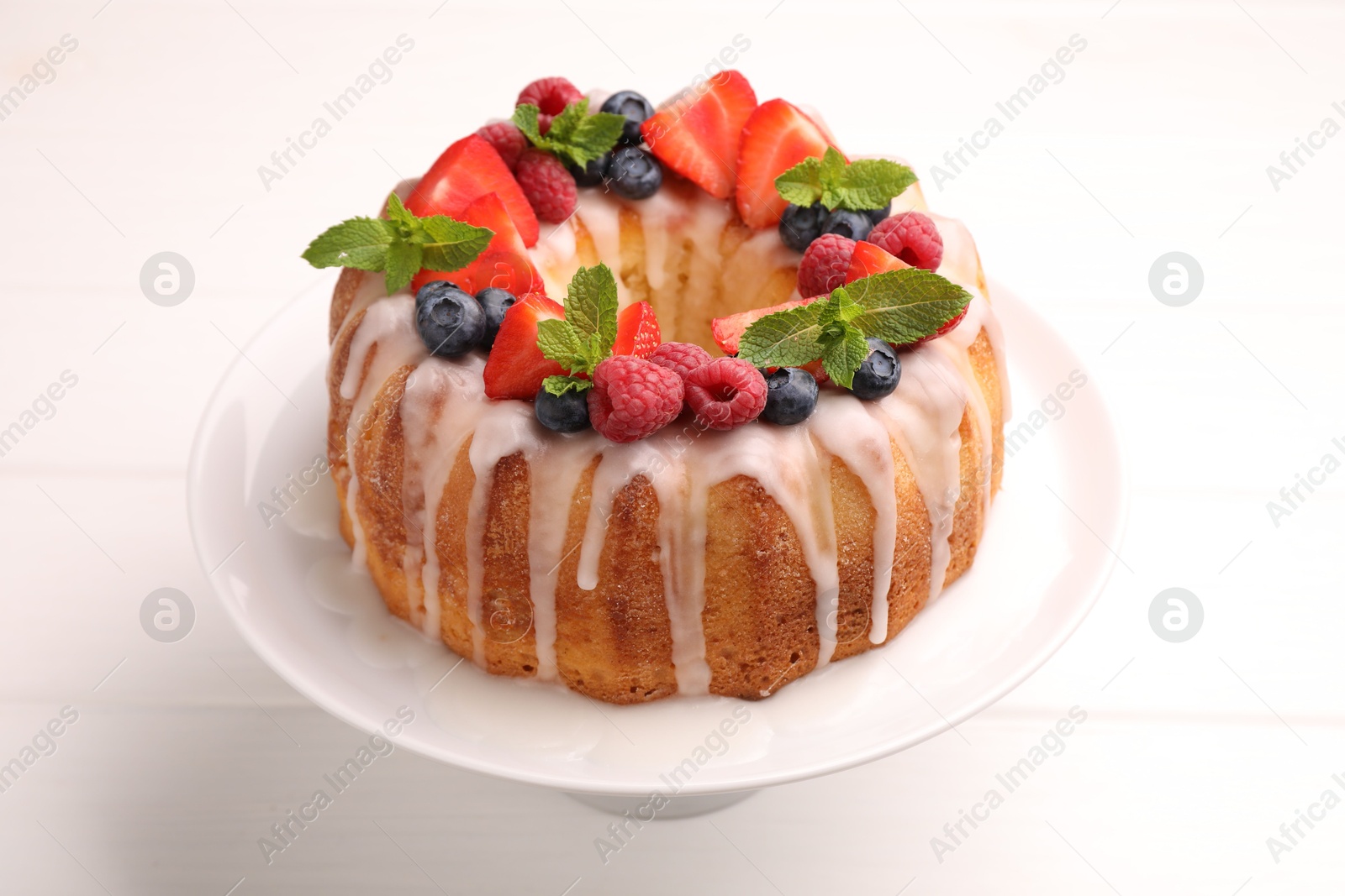 Delicious bundt cake with berries, glaze and mint on white wooden table, closeup Photo of Delicious bundt cake with berries, glaze and mint on white wooden table, closeup