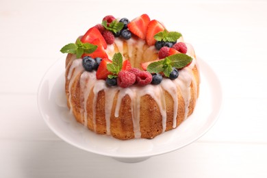 Photo of Delicious bundt cake with berries, glaze and mint on white wooden table, closeup