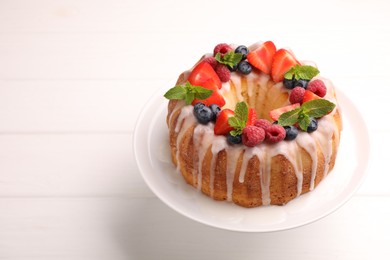 Photo of Delicious bundt cake with berries, glaze and mint on white wooden table, closeup. Space for text