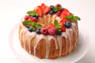 Photo of Delicious bundt cake with berries, glaze and mint on white table, closeup