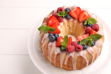 Photo of Delicious bundt cake with berries, glaze and mint on white wooden table, closeup