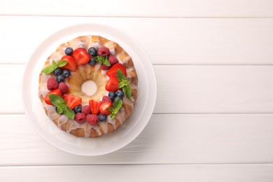 Photo of Delicious bundt cake with berries, glaze and mint on white wooden table, top view. Space for text