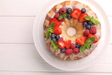 Photo of Delicious bundt cake with berries, glaze and mint on white wooden table, top view. Space for text